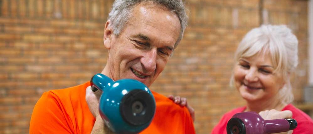 Aktiv ins neue Jahr - Zwei gut gelaunte ältere Menschen trainieren gemeinsam mit Hanteln – ein motivierendes Bild für die ‚Bring-a-Friend‘-Aktion unseres Fitnessstudios in Pirna.