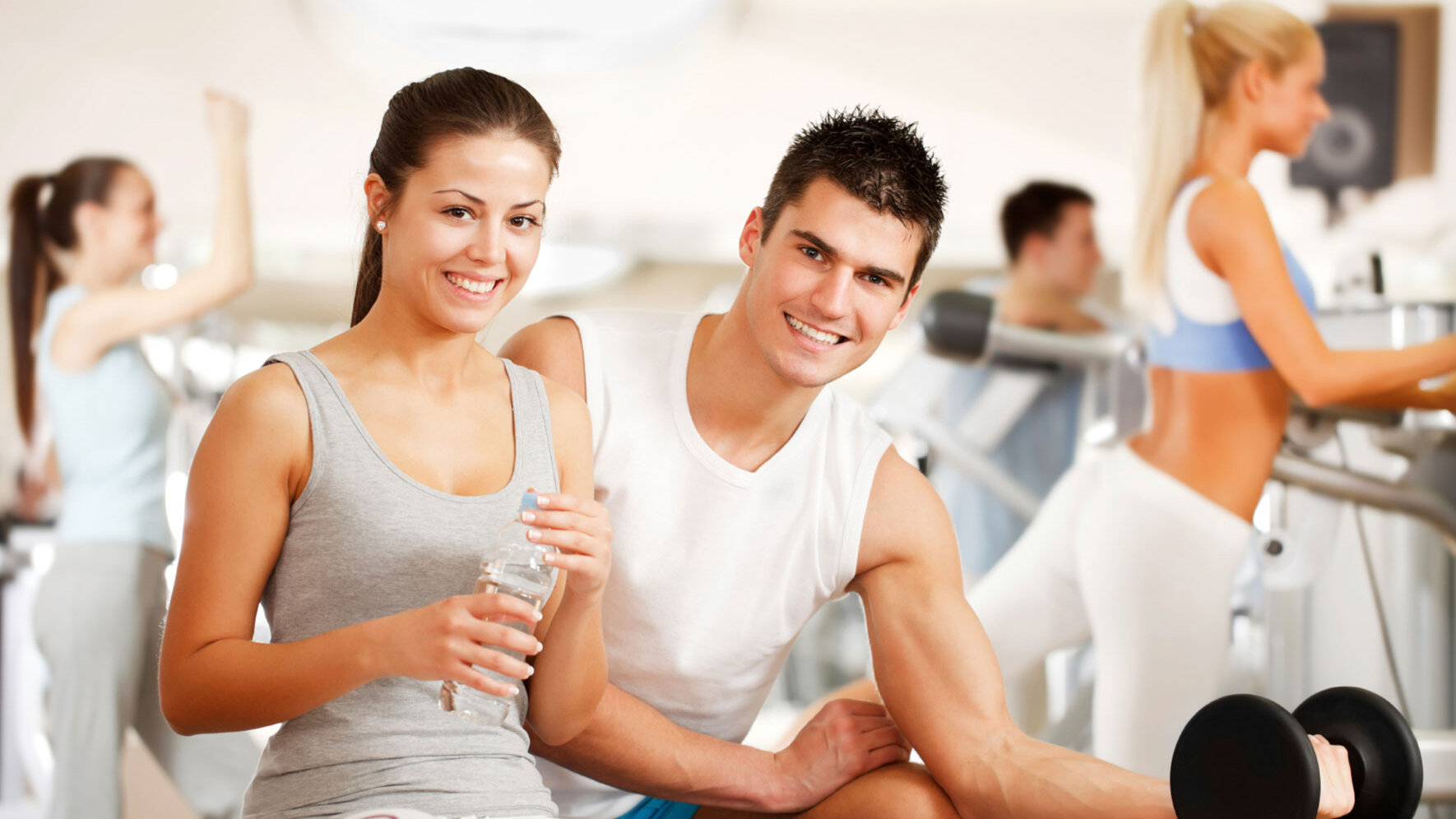 Mehrere Menschen trainieren gemeinsam in einem Fitnessstudio. Im Vordergrund stehen eine junge Frau und ein junger Mann, die lächeln und an Fitnessgeräten trainieren. Die Szene vermittelt Freude an Bewegung und einen aktiven, gesundheitsorientierten Lebensstil – passend zum Konzept ‚Abnehmen ohne Diät‘.