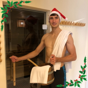 Junger Mann mit Nikolausmütze und einem weißen Handtuch über der Schulter steht im Aktiv Sporthotel Pirna vor einer verglasten Saunatür. Er hält einen hölzernen Saunakübel und eine Kelle in der Hand, als würde er einen Aufguss vorbereiten. Das Bild ist festlich mit digitalen Stechpalmen-Zweigen in den Ecken verziert und bewirbt die Nikolaussauna.