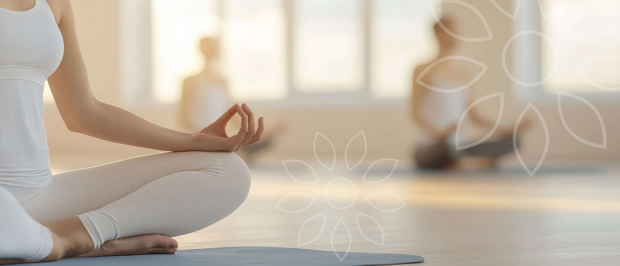 Eine Person sitzt in bequemer weißer Kleidung im Schneidersitz auf einer Yogamatte und hält die Hände in einer Meditationshaltung. Der Raum ist hell und ruhig, mit weichen Lichtreflexen. Im Hintergrund sitzen weitere Personen entspannt auf ihren Matten. Die Atmosphäre wirkt friedlich, zentriert und einladend – ideal für ein Wohlfühl-Retreat.