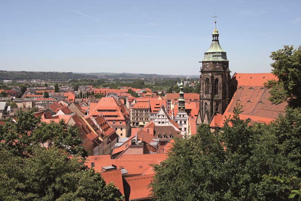 Die Skyline der Stadt Pirna: Historische Häuserdächer und der markante Turm der Marienkirche im Hintergrund.