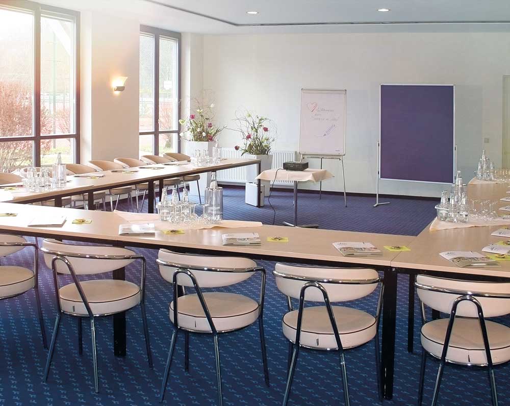 Moderner, heller Tagungsraum im Aktiv Tagungshotel Pirna mit großem Konferenztisch, komfortablen Stühlen, Präsentationstechnik und viel Tageslicht für professionelle Meetings