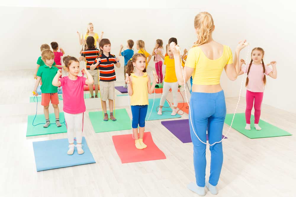 Gruppe von Kindern bei Aufwärmübungen vor dem Tennistraining - Trainerin im Vordergrund gibt Anweisungen 