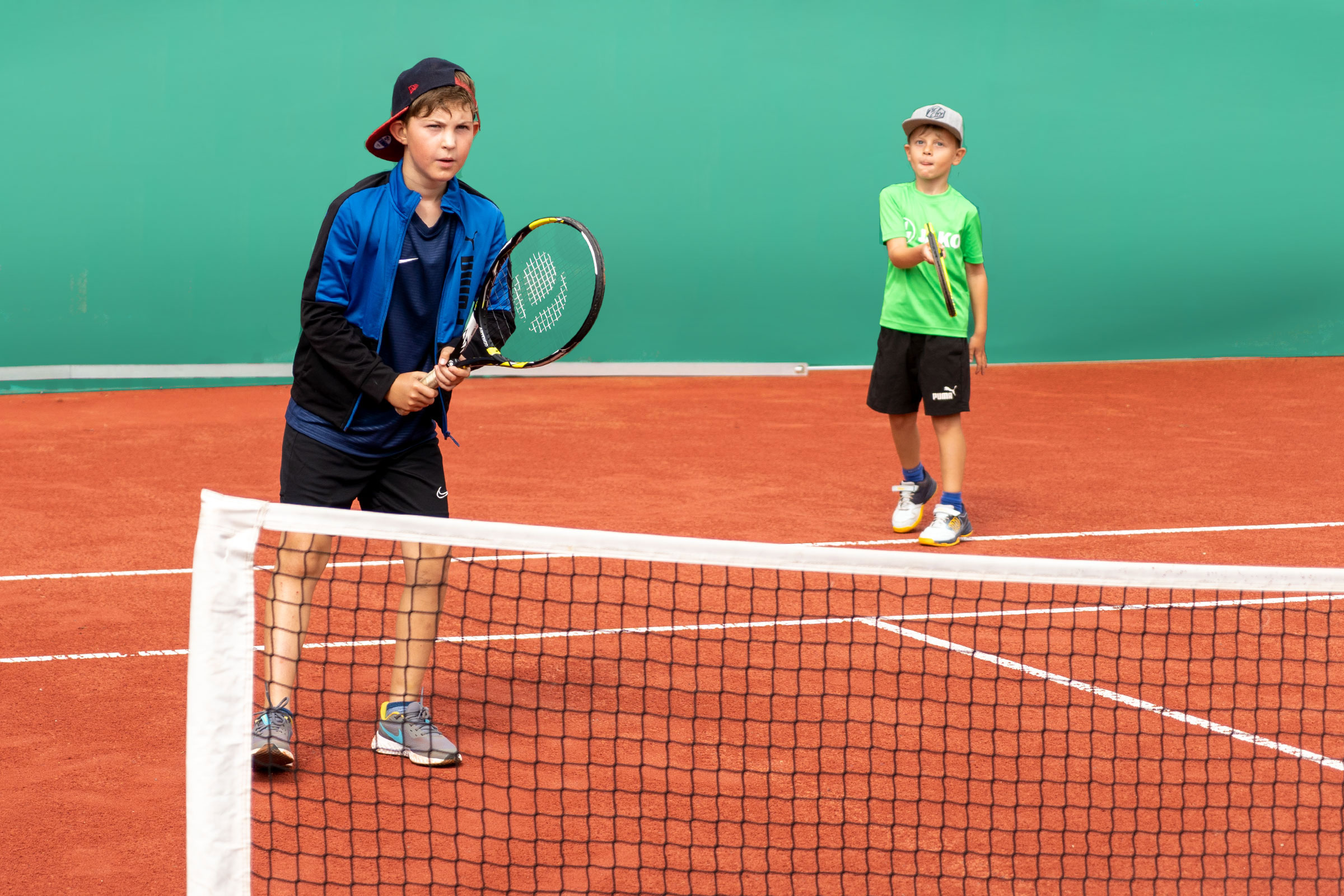 Zwei Kinder spielen Tennis auf einem Sandplatz, konzentriert beim Schlag am Netz – sportliches Training in der Tennusschule PRO4TENNIS