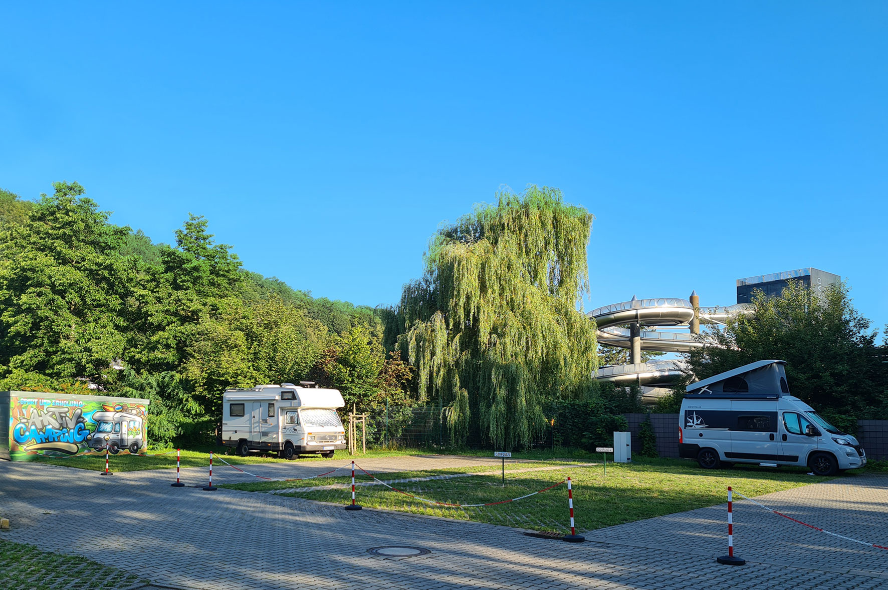 Großzügiger Wohnmobilstellplatz am Hotel in Pirna, Sächsische Schweiz: Befestigte Stellflächen im Grünen mit Blick auf geparkte Camper.