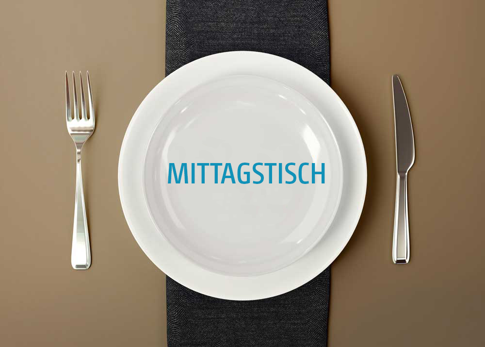 Weißer Teller mit der blauen Aufschrift Mittags­tisch, darauf liegend auf einem dunklen Tischläufer. Links daneben liegt eine Gabel, rechts ein Messer. Der Hintergrund ist in warmen Braun- und Beigetönen gehalten.